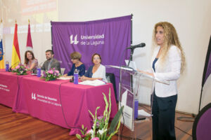 La directora del Servicio de Deportes, Begoña López, lee en pie la memoria del curso que termina, al lado de la mesa presidencial con la presencia de la consejera insular del Área de Educación, Juventud, Museos y Deportes, Concepción María Rivero Rodríguez; el rector, Francisco García Rodríguez; la vicerrectora de Sostenibilidad e Infraestructuras, Candela Díaz García; y la tesorera de la Asociación Alumni ULL, Mª Dolores Mejías Pérez.